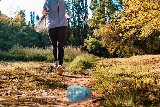 Person in sportswear jogging at the park and holding a bag of garbage. Bottom view. The concept of plogging, environment protection and volunteering