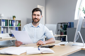 Obraz premium Young male businessman. Accountant, economist, financier. Works with documents, papers, reports, schedules. Sitting at his desk at the computer