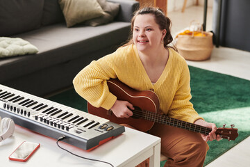 Modern young Caucasian woman with Down syndrome spending time at home enjoying playing guitar