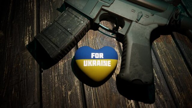 A steel weapon lies on a wooden table, next to it lies a plush heart in the yellow-and-blue tones of the Ukrainian flag.