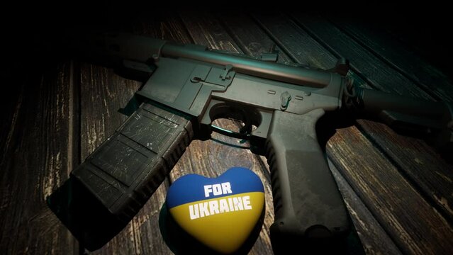 A steel weapon lies on a wooden table, next to it lies a plush heart in the yellow-and-blue tones of the Ukrainian flag.