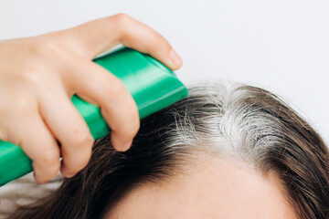 Naklejka premium Girl applying dry shampoo spray on roots of dark fluffy hair.