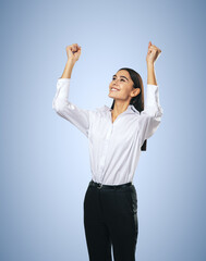 Joyful and satisfied woman in white shirt with raised hands showing her power, winner and...
