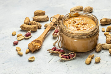 Peanut butter or paste in an open jar and peanuts in the peel scattered on a light background, banner, menu, recipe place for text, top view