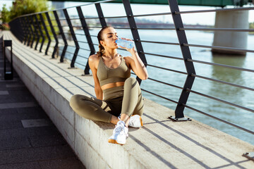 Fototapeta na wymiar Young woman taking a break during exercise on the river promenade