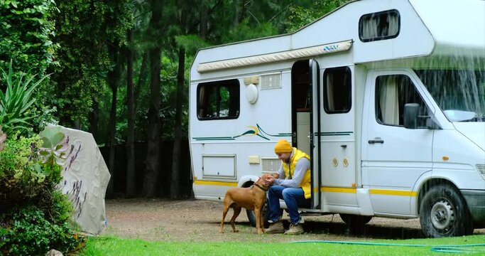 Young stylish american guy,man traveling in camper,house on wheels,trailer,motor home. a man with a dog prepares a basket of food for travel. Romantic road travel,freedom life,Millennial travel trend