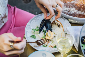 woman in pink shorts removing mussel from shell at dinner table with her hands