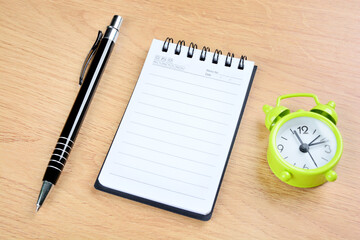 Alarm clock, notepad and pen on a wood background