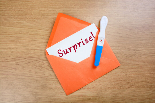 Positive pregnancy test in orange envelope on a wood background