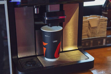 A cardboard cup of coffee is prepared using a coffee machine at a gas station.
