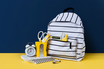White black striped backpack with school stationery on yellow and blue background. Office supplies...