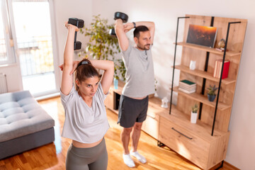 Couple doing tricep exercises using dumbbells