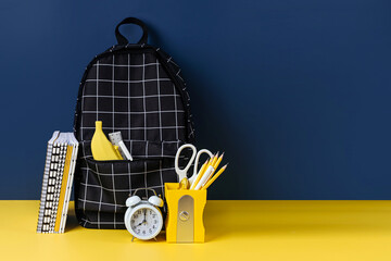 Black plaid backpack with school stationery on yellow and blue background. Office supplies with school bag on the table. Concept back to school.