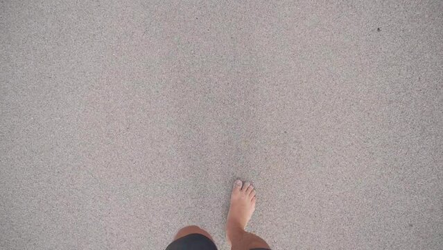 POV first person view looking at the ground walking backwards in the sand with bare feet in the daytime