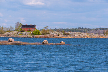 An old red wooden cottage standing on a rocky island. A small skerry and a swan in the foreground