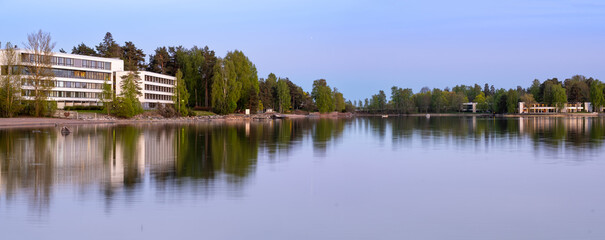Panoramic view of a bay of water. Trees and buildings cast reflections on the calm sea.
