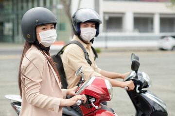 Fototapeta na wymiar Asian young man and woman wearing medical masks and protective helmets when riding scooters in city