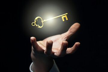 businessman's hand catches or holds an old golden glowing key, grab luck, key to success concept