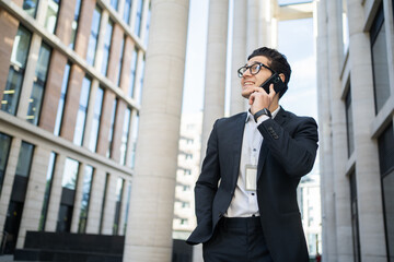 A man in glasses and a formal suit is a businessman talking on the phone with a client