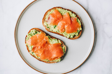 Toasted bread with mashed avocado and smoked salmon on grey plate