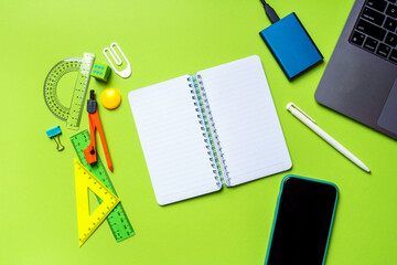 Back to school flat lay with a copy space. Empty mockup notepad and school supplies on a green background. Top view.
