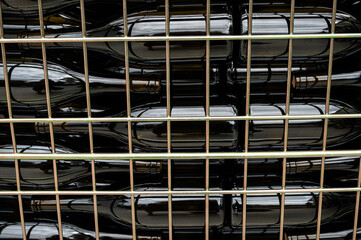 Profile view of full wine bottles lying in a container, freshly corked. In the foreground, the fence of the container.