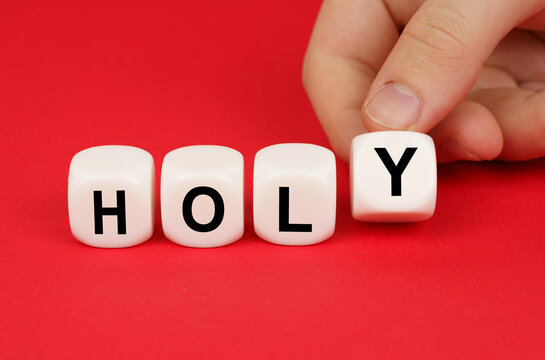 On a red background, a person's hand moves the cubes with the inscription - Holy