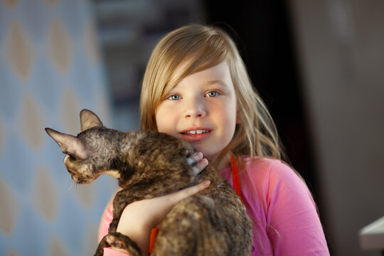 Portrait of a smiling girl with a Cornish rex cat in her arms.