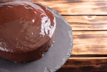 Carrot cake, covered in chocolate on stone surface over rustic wood, selective focus.