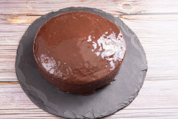 Carrot cake, covered in chocolate on stone surface over rustic wood, selective focus.