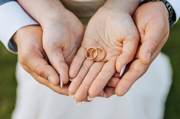 The bride and groom hold round gold rings in their hands, close-up on the palms. Wedding portrait, photography.