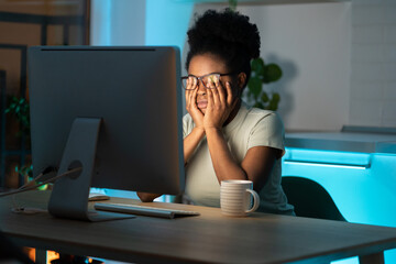 Symptoms of overworking. Young tired overworked african woman freelancer in eyeglasses working late from home, sitting in front of monitor, feeling eye strain and fatigue during computer work.  - Powered by Adobe