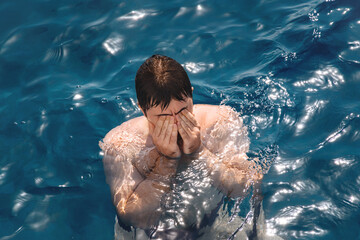 Man in the blue water of the pool or in the sea. The guy touches his face with his hands after...