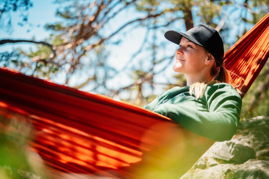 Woman with cap resting in comfortable hammock in mountains. Relaxing on orange hammock between two trees pine enjoying the nature view
