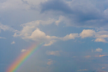 White clouds and colorful rainbow against blue sky. Daylight, cloudy day. Nature, freedom and peaceful concept