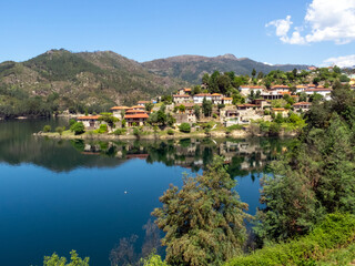 Fototapeta na wymiar Paisaje con casas reflejándose en el agua de un río. Río Cávado, Parque Natural do Gêres, norte de Portugal.