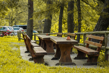Naklejka premium Wooden seats and bench in a park meant for rest for hikers bikers and other travelers. Typical outside equipment of mountain lodge.