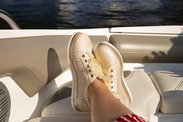 female legs in beige sneakers with yellow bows on seat of yacht close-up
