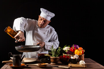 Male chef in white uniform pouring vinegar onto the cooking pan
