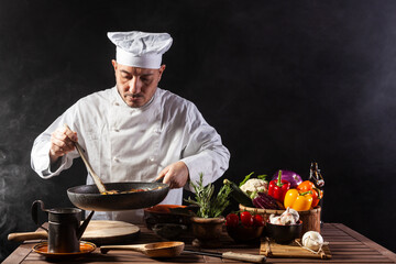 Male cook in white uniform and hat with ladle mixes the ingredients onto the cooking pan