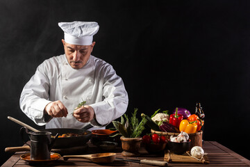 Male cook in white uniform and hat putting herbs on food plate with vegetable