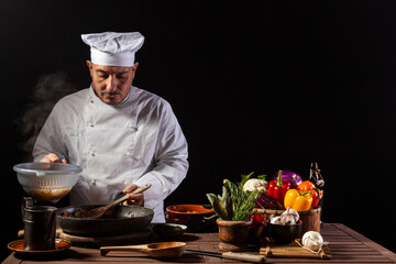 Male chef in white uniform pouring boiled spaghetti into pan wok for cooking pasta with vegetables.