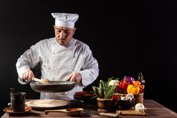 Male cook in white uniform and hat with ladle mixes the ingredients onto the cooking pan