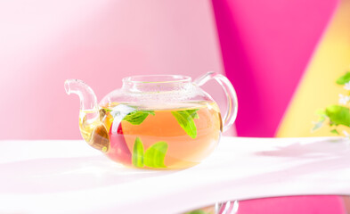 Glass teapot with fresh mint tea on light pink background