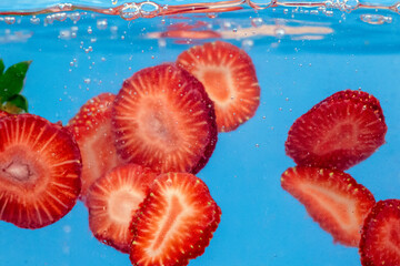 Sliced Strawberry in water with water splash and air bubbles on blue background. Close up image.
