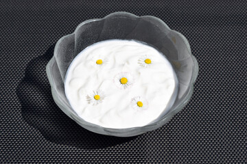Glass bowl with fresh plain yogurt, decorated with daisy flowers
