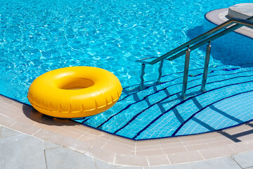 Yellow ring floating in refreshing blue swimming pool - obrazy, fototapety, plakaty