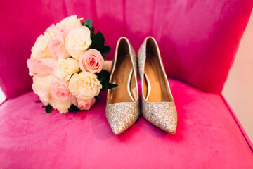 Elegant bridal sparkle silver shoes on a pink chair with wedding bouquet 