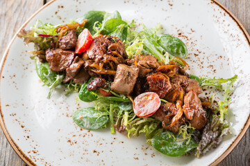 Warm salad with grilled chicken liver, cherry tomatoes and mushrooms in ceramic plate on wooden table.