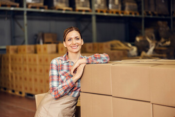 A food factory worker posing with boxes in warehouse and smiling at the camera.